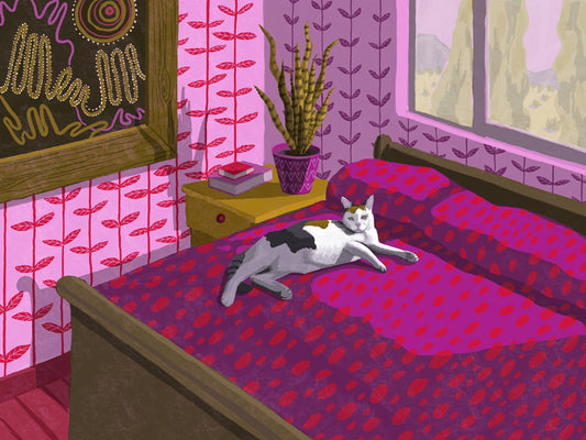 A dilute calico cat reclines on a bed in the sunshine in a room of rich reds and pinks patterning the bedspread and walls.