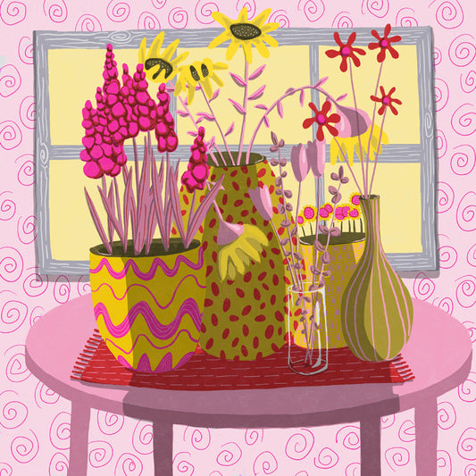 Whimsical pink and yellow flowers sit atop a pink table in a pink room in front of a window with light streaming into the room